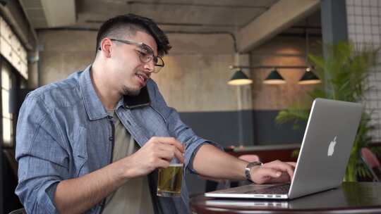 一个男人一边打电话一边用笔记本电脑喝啤酒