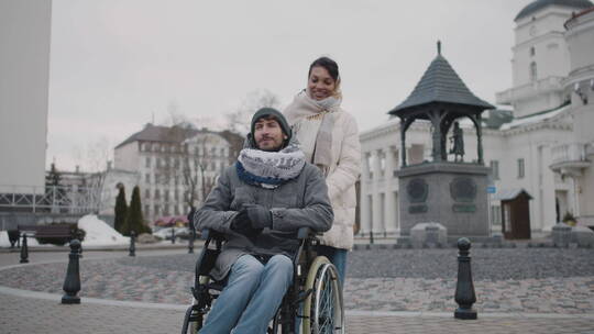 女人推着坐轮椅的男人散步视频素材模板下载