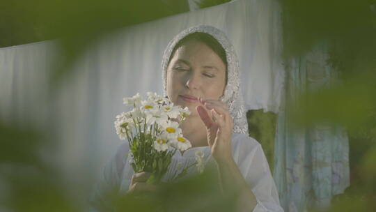 头戴白色披肩的女性撕着雏菊花瓣