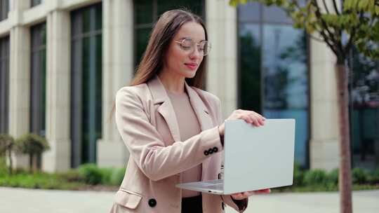 女性在当代建筑背景下摆姿势时关闭笔记本电