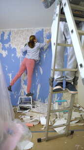 一名年轻女子小心翼翼地从墙上取下旧壁纸