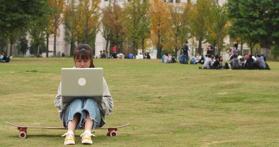 大学校园里女大学生坐在滑板上用电脑学习