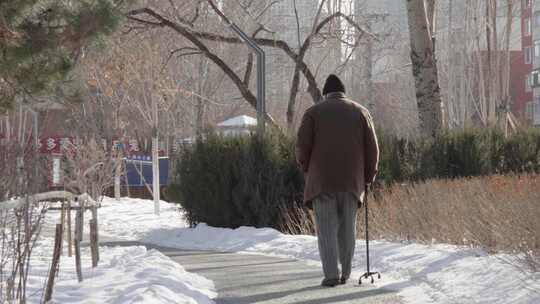 拄拐老人在雪地小路上行走