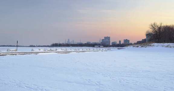 冰冻的湖面被雪覆盖，远处有一座城市