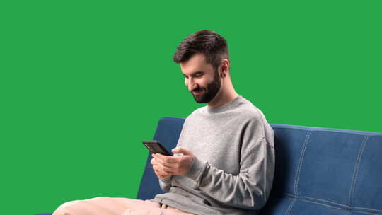 微笑的男人浏览互联网聊天社交网络沙发上的智能手机色度键绿屏