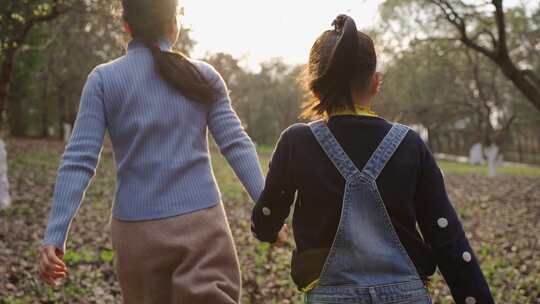 小女孩和妈妈牵手走在公园散步背影亲子陪伴
