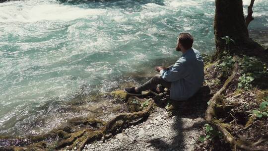 坐在河边的男士看着急速的水流流过