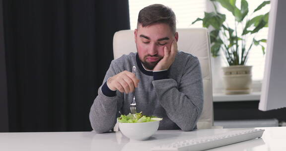 不快乐的人坐在办公桌前吃健康沙拉