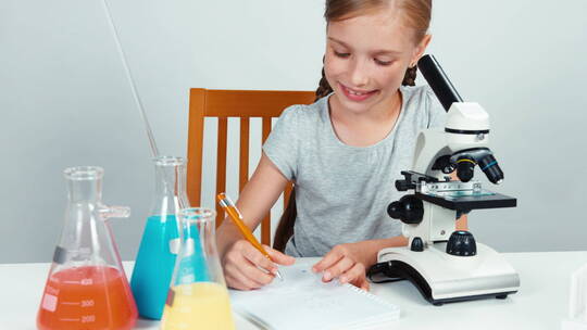 女孩使用显微镜在她的练习册上写作业