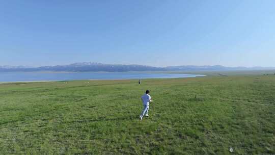 航拍男子奔跑在夏天赛里木湖畔的草地上