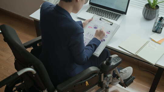 坐轮椅在笔记本电脑前检查商业文件的女专家