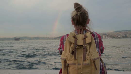 坐在海湾岸边看天空彩虹的女游客