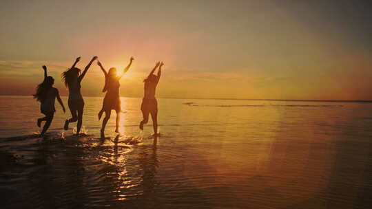 四个十几岁的女孩跑进水里，在日落时分的海滩上庆祝。海滩派对。太阳