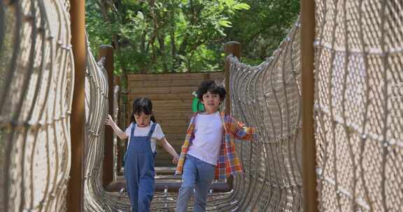两个小孩子相互鼓励牵手走绳桥