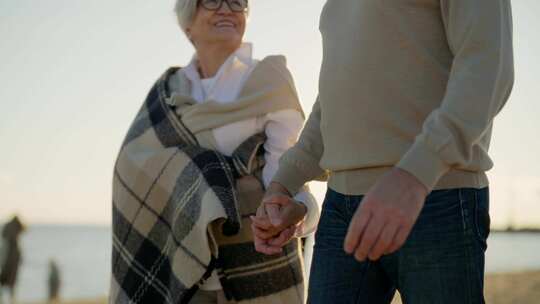老年夫妇走在沙滩上说话微笑拥抱休息爱妻子