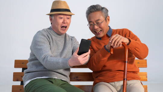 两位老年朋友坐在长椅上使用手机
