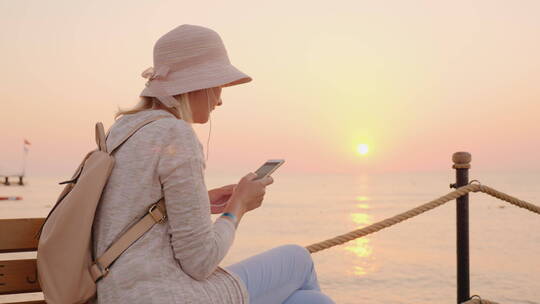 海边夕阳下玩手机的女孩
