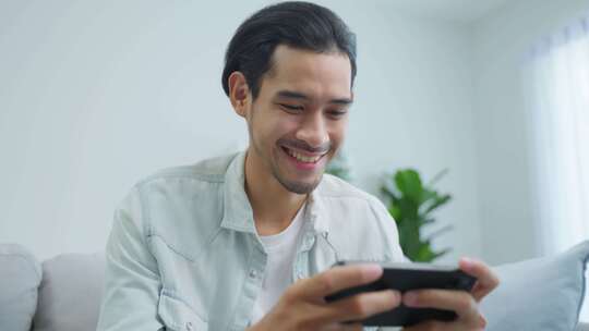 亚洲年轻英俊的男子玩家在家用智能手机玩手机游戏。