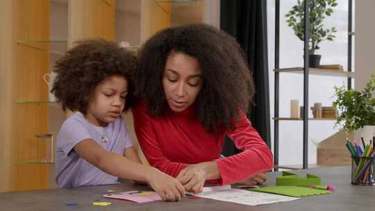 可爱的学龄黑人女孩在母亲的帮助下制作面料