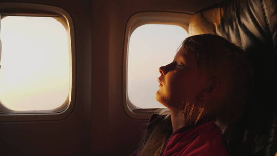 夕阳下飞机上的女孩在窗户旁睡觉