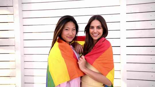 女同性恋夫妇一边看着相机一边用彩虹旗拥抱