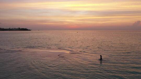 与一名女子在日落时散步的海滩鸟瞰