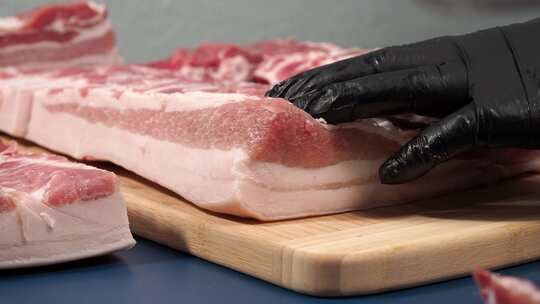 一个戴黑手套的男人在砧板上切猪肉。