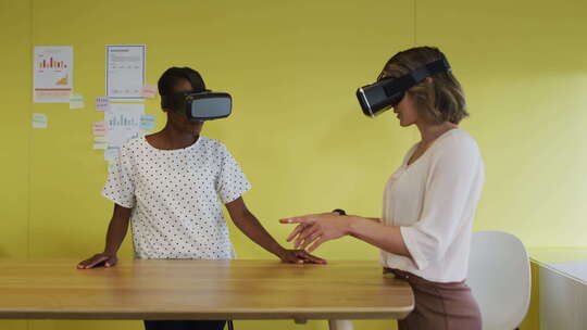 两个不同的女同事站在办公桌前，测试虚拟现实谷歌