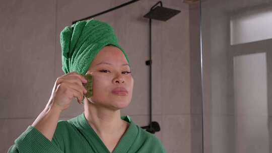 中年亚洲妇女使用玉刮砂面部工具进行水疗治