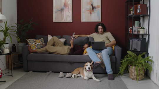 跨种族年轻夫妇与狗放松在沙发上在家里