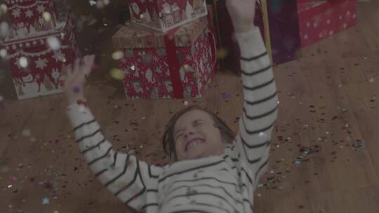 头戴圣诞帽的小男孩快乐的躺地上玩彩纸礼花