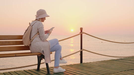 坐在长椅上看海上日落的女人