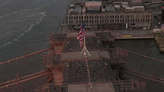 美国航空公司：纽约布鲁克林大桥上空有美国国旗和雾蒙蒙的曼哈顿上空的特写圆圈飞行