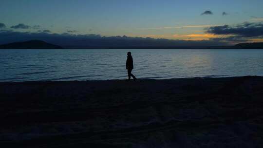 夕阳下一个人在海滩上行走剪影