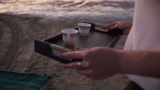 一个女孩端着托盘，托盘里有咖啡和茶杯，准