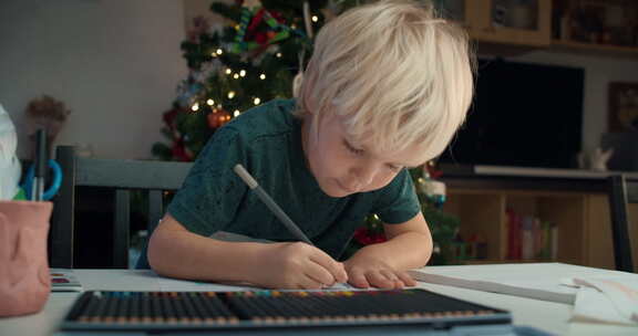 圣诞假期坐在桌旁用铅笔画画的可爱儿童男孩