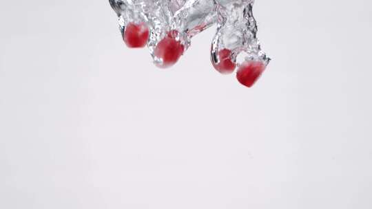 红色石榴籽落入水中，白背景 慢镜头