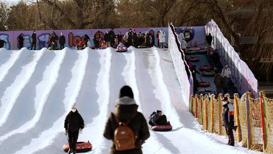 4K升格实拍冬季在冰雪乐园玩雪圈滑梯的游人