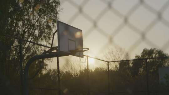 日落时分隔着球场外网的篮球框
