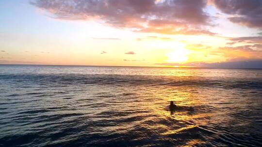 女子在风平浪静的海面上划着冲浪板进入日落