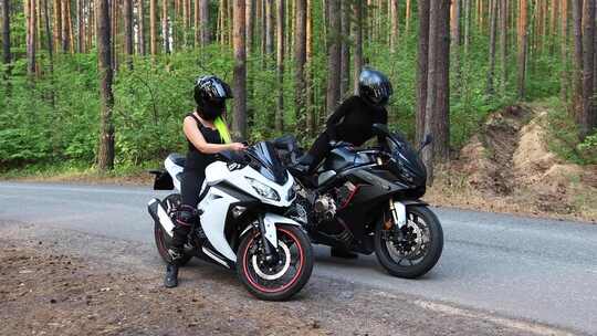 森林里的摩托车两个女人从摩托车上下来，摘下头盔
