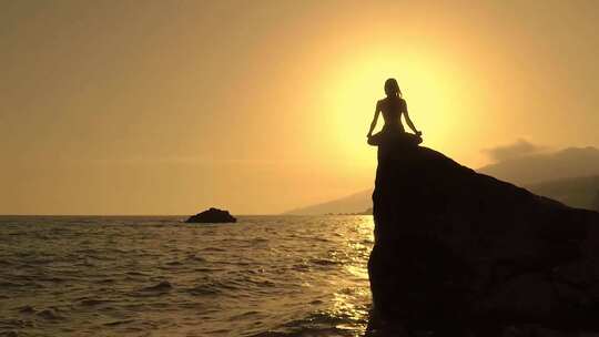 夕阳下女孩在海边岩石上打坐冥想