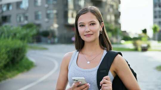 年轻漂亮的女人用智能手机背包摆姿势户外城