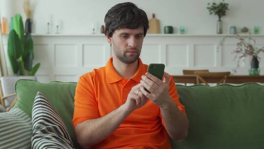 男人坐在沙发上拿着手机兴奋激动地欢呼视频素材模板下载