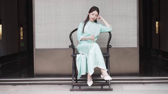 年轻旗袍女子摇着扇在中式合院门廊椅子休息