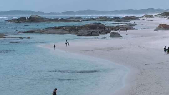 人们走在岩石海岸的白色沙滩上