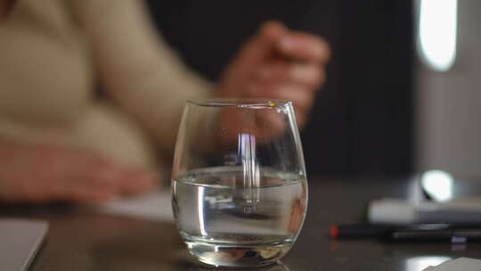 在前景中，一杯水放在桌子上，一个孕妇用刷
