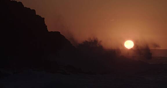 日落时巨浪拍打海岸的岩石