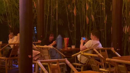 夜晚公园竹编椅喝盖碗茶玩手机的人们1视频素材模板下载
