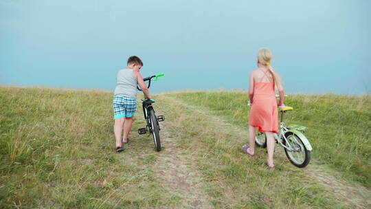 两个孩子推着自行车走在草地上